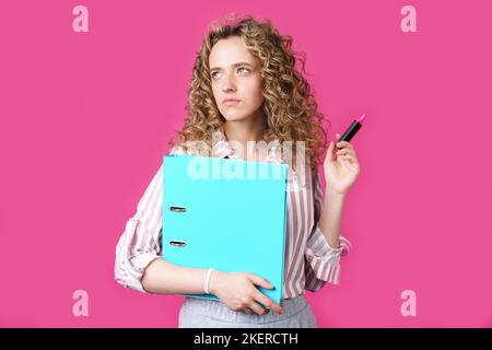 Fashionable woman in a striped shirt holding a folder with documents and a marker. Looks up. Isolated on pink background Stock Photo