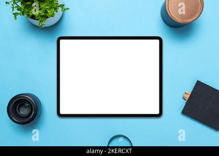 Tablet with isolated white display on blue table. Top view, flat lay composition. The plant, lens, box, magnifying glass and table beside Stock Photo