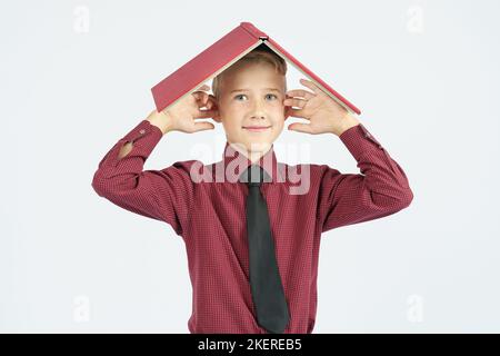 The schoolboy put an open book on his head and covered his ears with his fingers, isolated background. Education concept Stock Photo