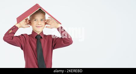 The schoolboy put an open book on his head and covered his ears with his fingers, isolated background. Education concept Stock Photo