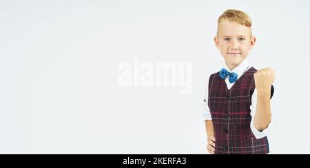 A portrait of a schoolboy who clenches his hands into a fist affirmatively, making a gesture. Isolated background. Education concept. Stock Photo