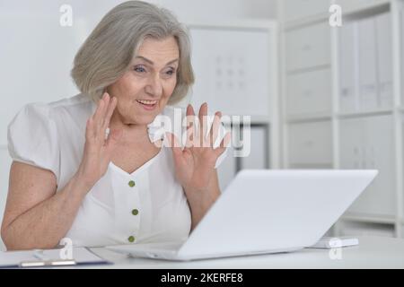 Elderly woman in headphones take online course on computer at home. Stock Photo