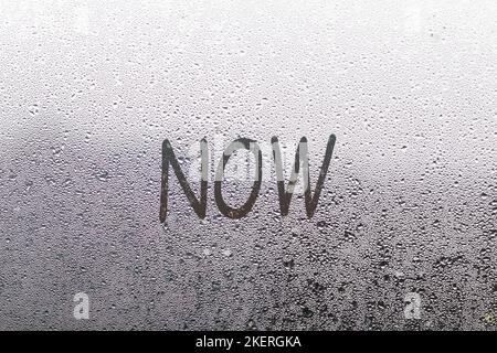 Handwritten lettering now on misted glass on window with raindrops, concept of full life and motivation Stock Photo