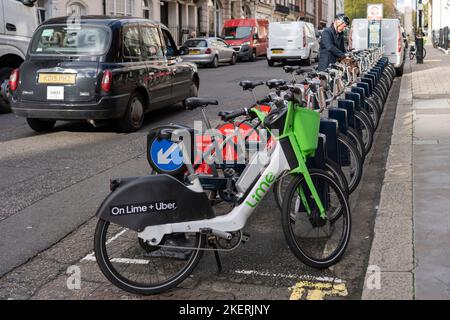 Uber + Lime and Santander sponsored electric bike hire in London. A cyclist picking picking a bicycle as a taxi passes. England Stock Photo