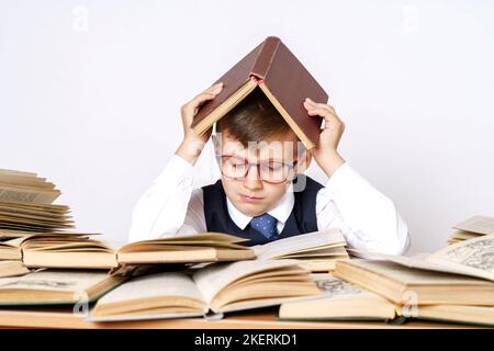 Education concept. The student does his homework, reads, put the book on his head. There are many open books on the table. Stock Photo