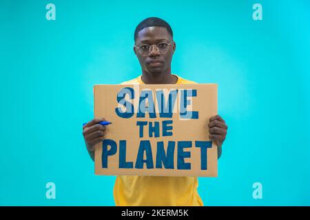 Young black man holding save the planet sign protesting climate change isolated on blue background. Stock Photo