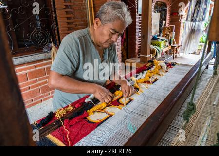A master weaver weaves a woolen rug on a wooden foot treadle loom in the family weaving business in Teotitlan, Oaxaca, Mexico.  The weaver's name is J Stock Photo