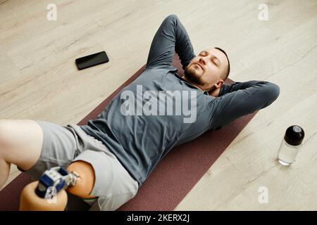 Top view of man with prosthetic leg doing exercises at home on yoga mat Stock Photo
