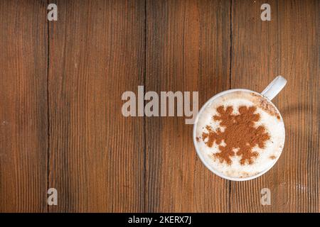 Cappuccino, hot chocolate latte coffee with snowflake pattern on warm wooden background, cup with hot chocolate drink in woman hands, top view copy sp Stock Photo