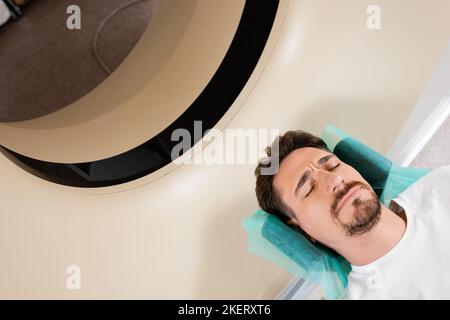 high angle view of tense brunette man with closed eyes doing diagnostics on computed tomography scanner,stock image Stock Photo