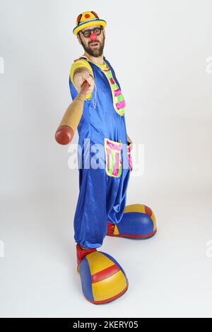 Holiday concept. The clown is a man in a bright blue and yellow suit with a baseball bat. Stock Photo