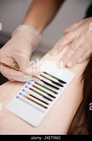 Close up of female hands in sterile gloves picking up volume lashes with stainless steel tweezers. Lash technician choosing eyelashes for lash extension procedure in beauty salon. Stock Photo