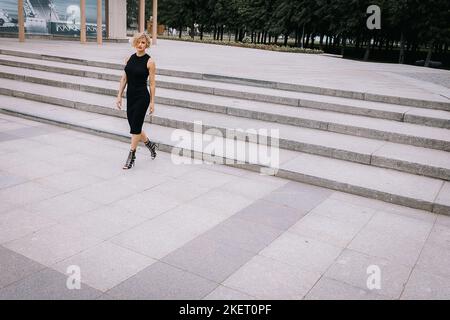 Beautiful woman in black clothes walks up stairs in park. Art shooting from unusual angles. High quality photo Stock Photo