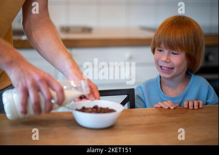 Man pouring milk into the plate of his son Stock Photo