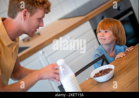 Man pouring milk into the plate of his son Stock Photo