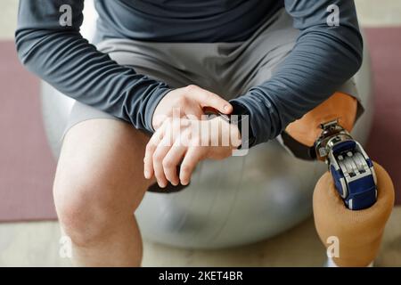 Close up of man with prosthetic leg checking smartwatch sitting on fitness ball during home workout Stock Photo