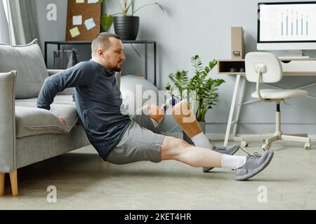 Side view portrait of man with prosthetic leg doing exercises at home in minimal interior Stock Photo