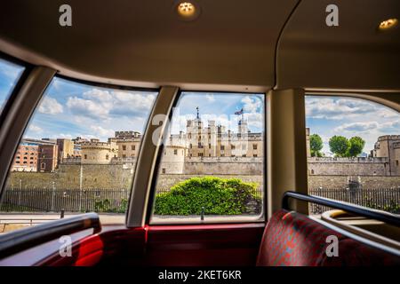 A routemaster Red London bus overlooks the tower of london.The image is taken through the windows of the bus, showing the Tower with union jack flack Stock Photo