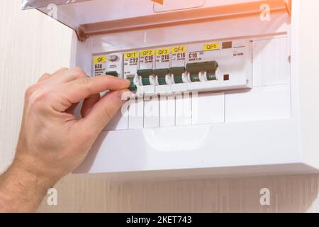 Circuit breaker board displays many switches. A finger is about to turn it back on. Stock Photo