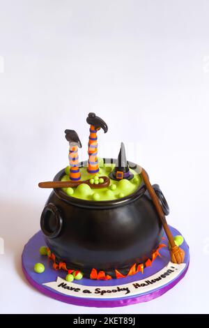 Fun and scary Halloween cake on white background. Witch hat, legs, and a wooden spoon on a black cauldron with bubbling green liquid. Broom on side. Stock Photo