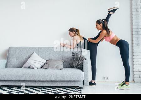Fit girls preparing legs workout. Leg stretching exercise fitness woman doing warm-up, hamstring muscles stretch standing at home Stock Photo