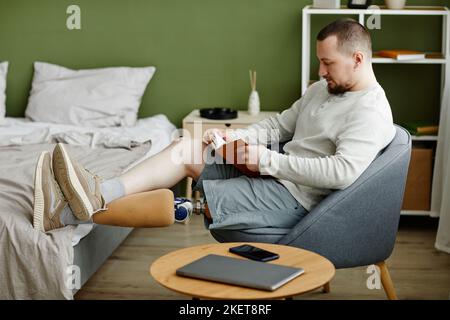 Side view portrait of man with prosthetic leg reading book at home and relaxing, copy space Stock Photo