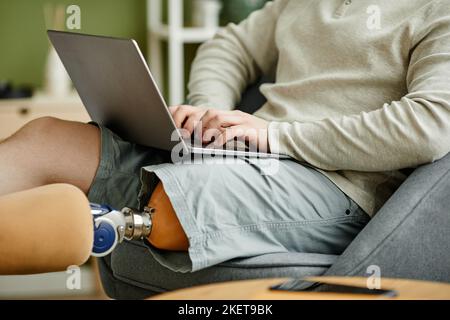 Close up of man with prosthetic leg using laptop while relaxing at home, copy space Stock Photo