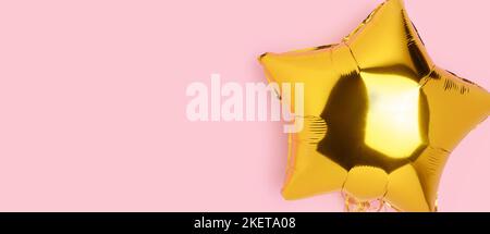 Banner with gold colored inflatable foil balloon in a star shape. Festive concept on a pink background with copy space. Stock Photo