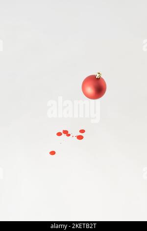 Red Christmas bauble decoration with drops of red paint on white backgorund. Minimal New Year concept. Stock Photo
