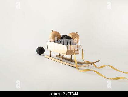 Gold colored wooden sleigh with Christmas baubles and decorative ribbon on white background. Minimal New Year concept. Stock Photo