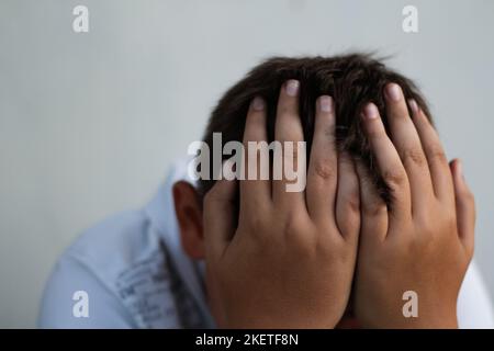 Defocus sad little boy sitting. Child cry and hiding his face. Kid alone. Victim of bulling. Problem in school. Social protection. Fatty child, weight Stock Photo