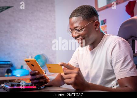 Young black man shopping online smiling happy holding mobile phone and credit card buy and pay Stock Photo