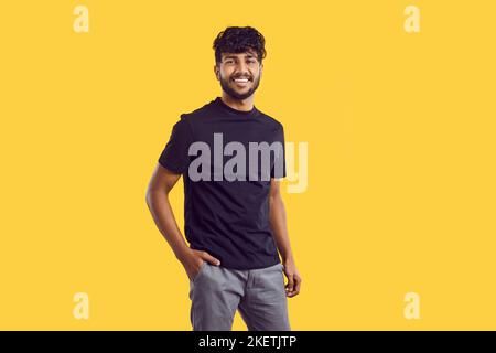 Young South Asian man with dark curly hair posing with smile in casual clothes stands in studio Stock Photo