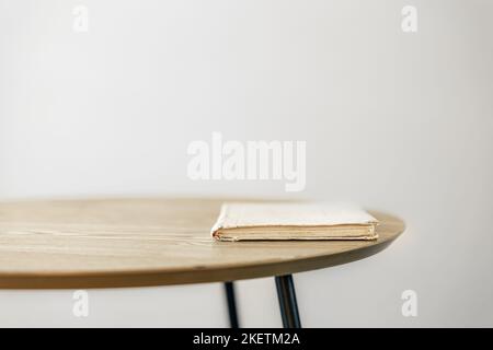 An old book on a small table against a white wall. Stock Photo