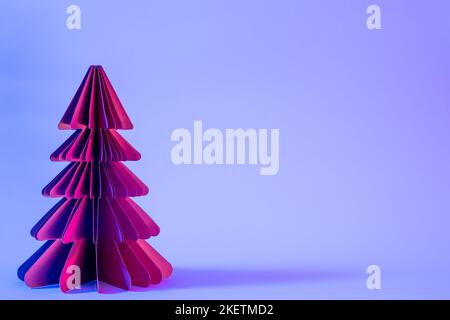 Decorative paper Christmas tree on blue background with trendy neon light. Stock Photo
