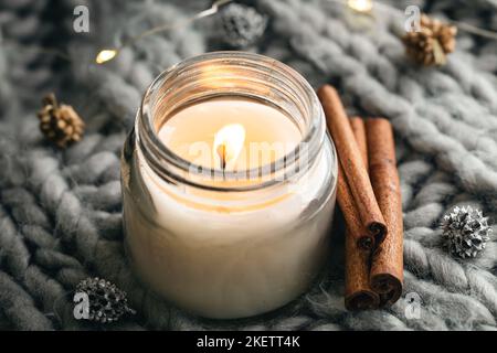 Close-up, candle and cinnamon sticks on the background of a gray knitted element. Stock Photo
