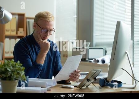 Pensive young architect examining blueprint in his hands Stock Photo