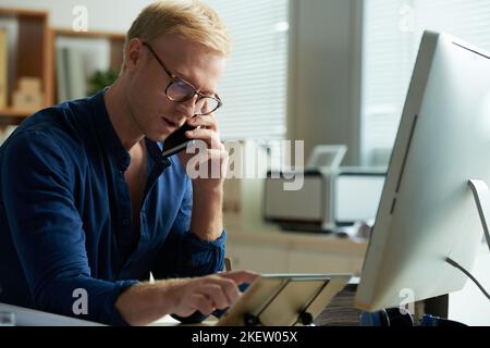 Young entreprneur in glasses using tablet computer and calling on phone Stock Photo