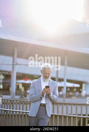 Old senior business man using smartphone standing in city outdoors. Stock Photo