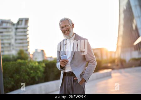 Cheerful old professional business man holding phone using mobile phone outdoor. Stock Photo