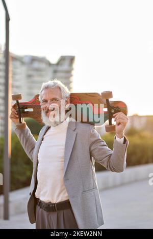 Active happy cool older business man skater holding skateboard in city. Stock Photo