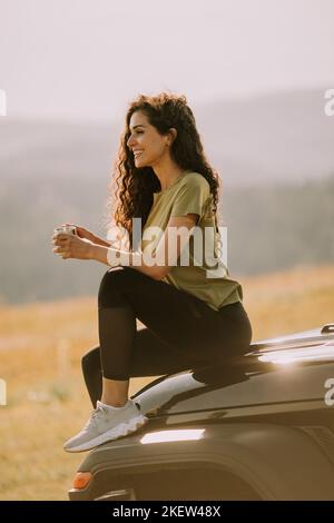 Pretty young woman relaxing on a terrain vehicle hood at countryside Stock Photo