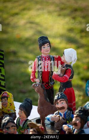 Assortment of clay souvenirs. Souvenir clay figurines of men and women in national Moldovan costumes. Moldavian folk art on Wine Day theme. Selective Stock Photo