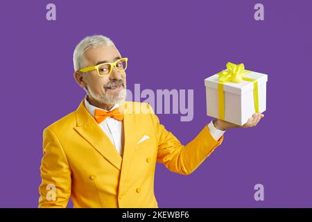 Happy senior man in yellow suit and glasses showing present box from holiday sale Stock Photo