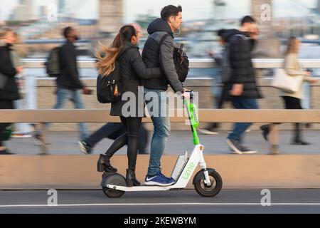 A couple riding on a Lime e-scooter part of the Transport for London e-scooter hire scheme, across London Bridge during rush hour.  London Bridge, Lon Stock Photo