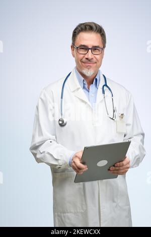 Middle age doctor in lab coat. Friendly physician, general practitioner with tablet. Mid adult, mature age man, happy smiling. Portrait isolated on white. Stock Photo