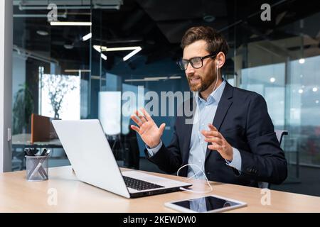 Online meeting, mature businessman inside office talking remotely online with colleagues and partners, video call senior male executive using laptop to communicate. Stock Photo