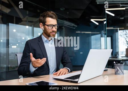 Online meeting, mature businessman inside office talking remotely online with colleagues and partners, video call senior male executive using laptop to communicate. Stock Photo
