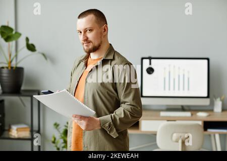 Waist up portrait of adult man looking at camera while standing in minimal office and holding document, copy space Stock Photo