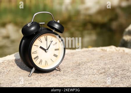 Vintage alarm clock on stone in park, closeup Stock Photo